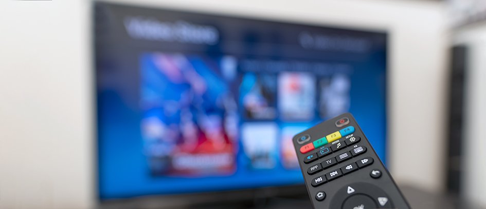 IPTV-käyttöliittymä näkyy televisiossa, etualalla kaukosäädin osoittaa kohti näyttöä, jossa näkyy digitaalinen ohjelmaopas.