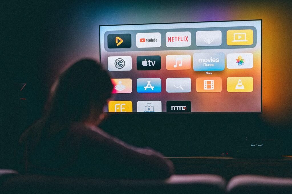 Apple TV:n kotinäyttö, jossa näkyy eri suoratoistopalvelujen kuvakkeet kuten YouTube, Netflix ja Apple TV - käyttäjä selaa IPTV-vaihtoehtoja.